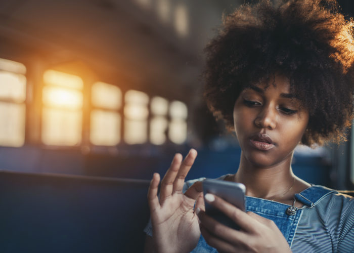 Cute mixed girl in train chatting via smartphone Thoughtful young biracial girl using smart phone while sitting alone in suburban train, curly african teenage female having online chat with her sister in train with copy space for your text or logo