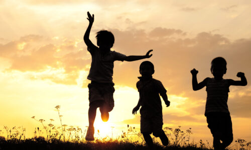 Children running on meadow at sunset