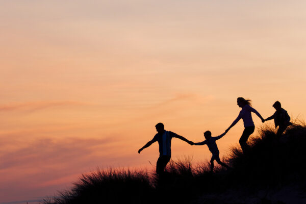 Silhouette of family running through the sand dunes at sunset.