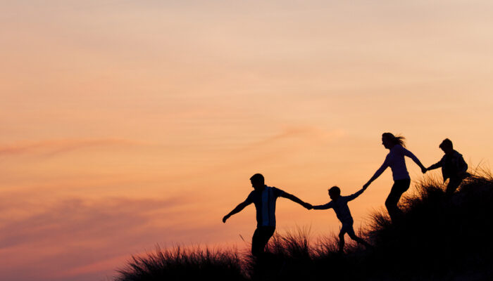 Silhouette of family running through the sand dunes at sunset.