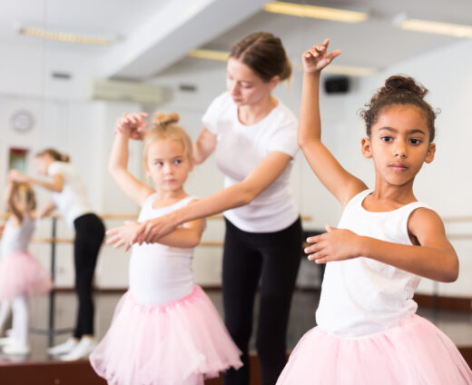 Dance teacher helping her little girls students Young female classical dance teacher helping her little girls students in ballet class